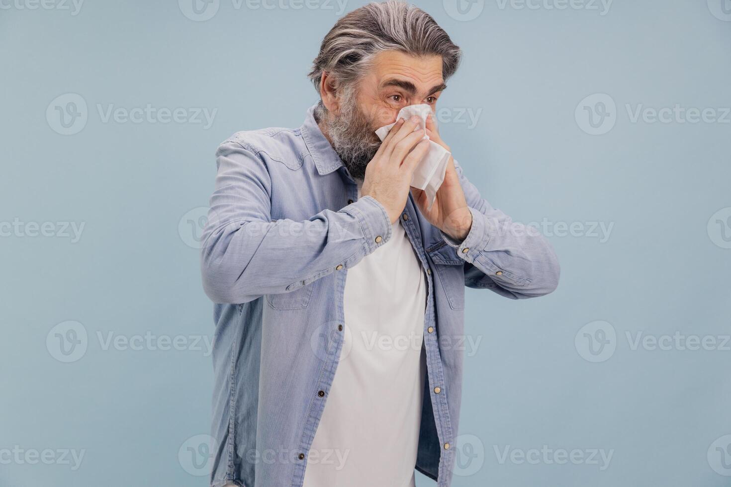 Senior Man Blowing Nose with Tissue on Blue Background photo