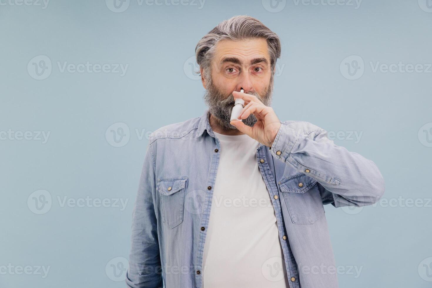 Senior man using nasal spray for treating rhinitis and preventing flu photo