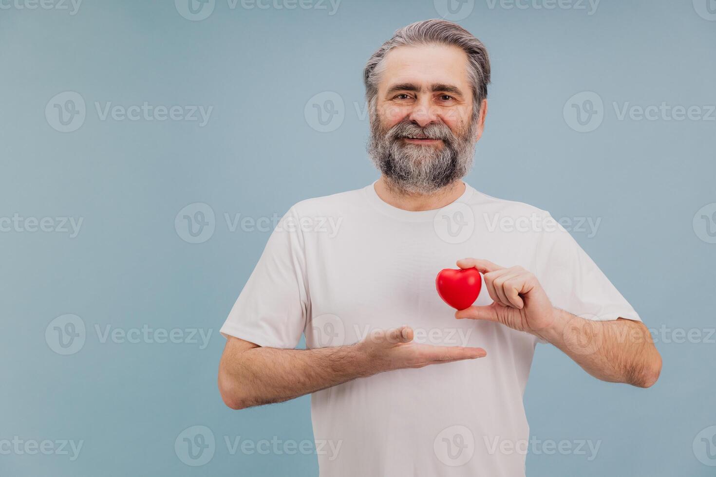 Smiling Senior Man Holding Small Red Heart Promoting Healthcare and Cardiology Awareness photo