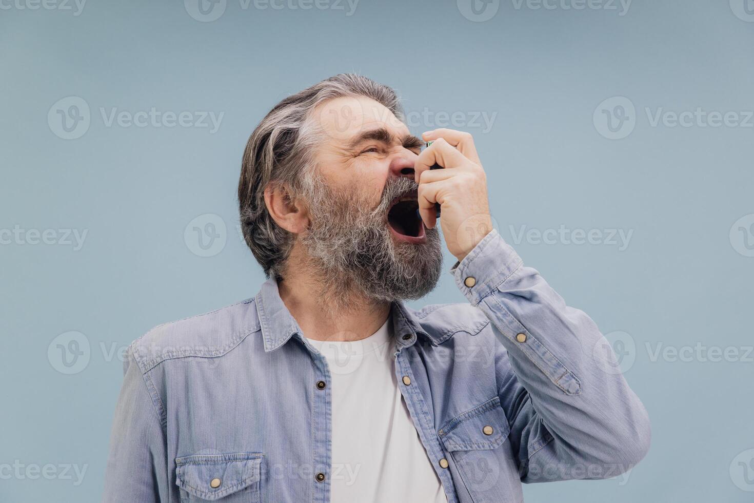 Senior man using a nasal spray for treatment on blue background photo