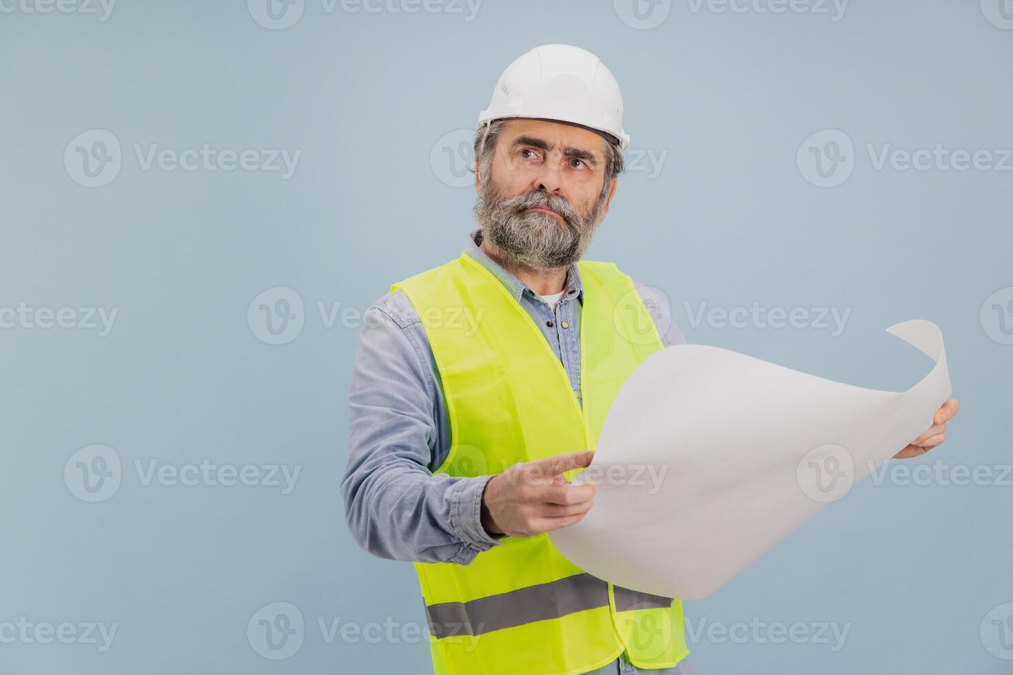 Senior engineer wearing safety helmet and vest pointing at blueprint on blue background photo