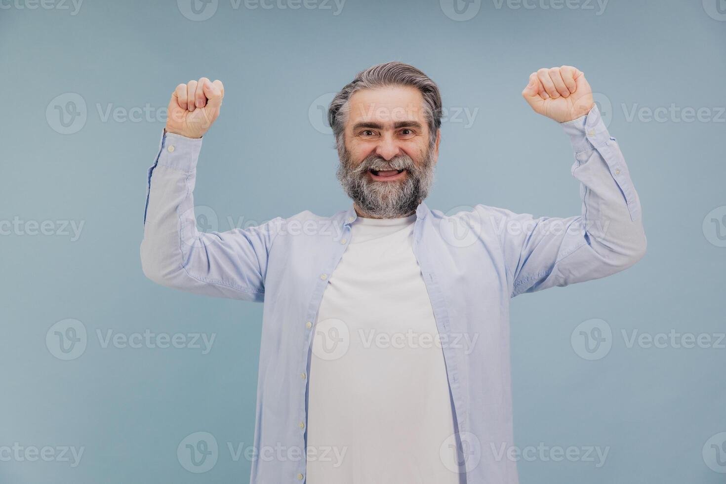 Senior man raising fists in victory celebrating success on studio background photo