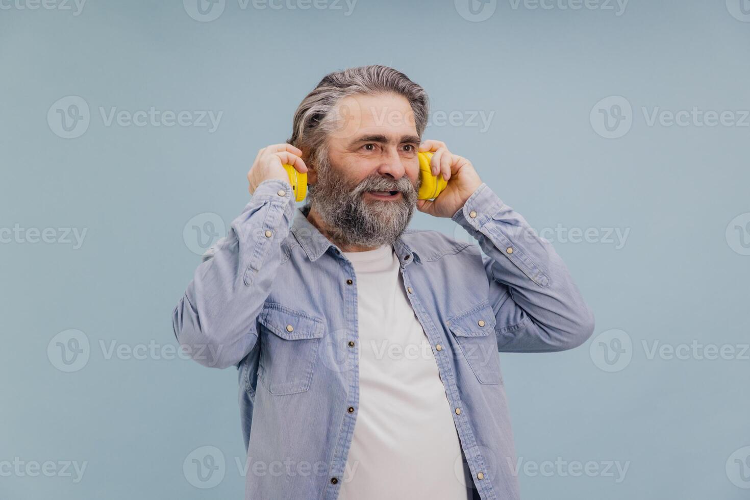Senior man enjoying music with yellow headphones on light blue background photo