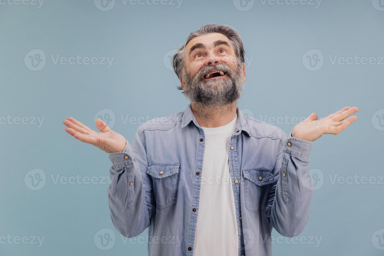 Surprised senior man shrugging shoulders with open palms looking up on blue background photo