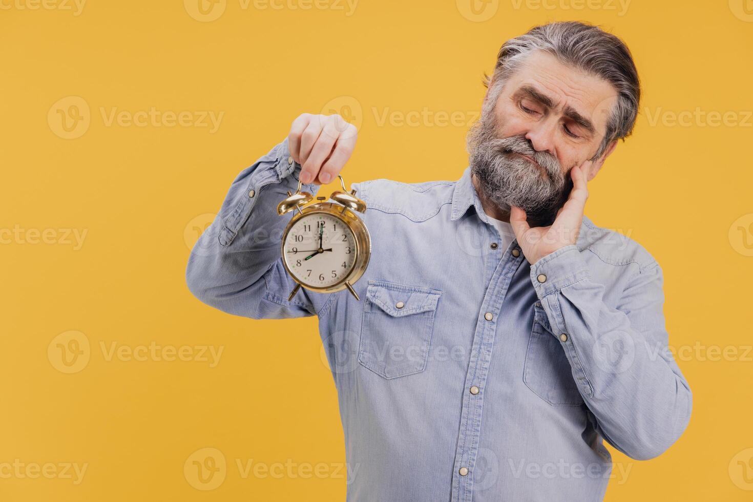 Sleepy senior man holding alarm clock and yawning on yellow background photo