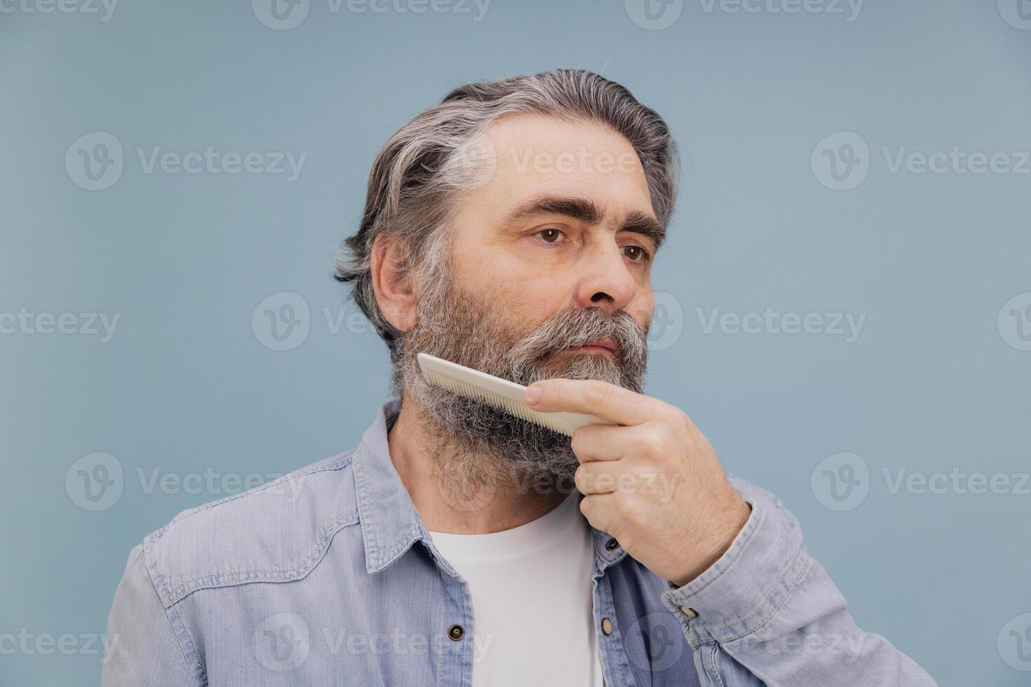 Senior man combing his beard on blue background photo