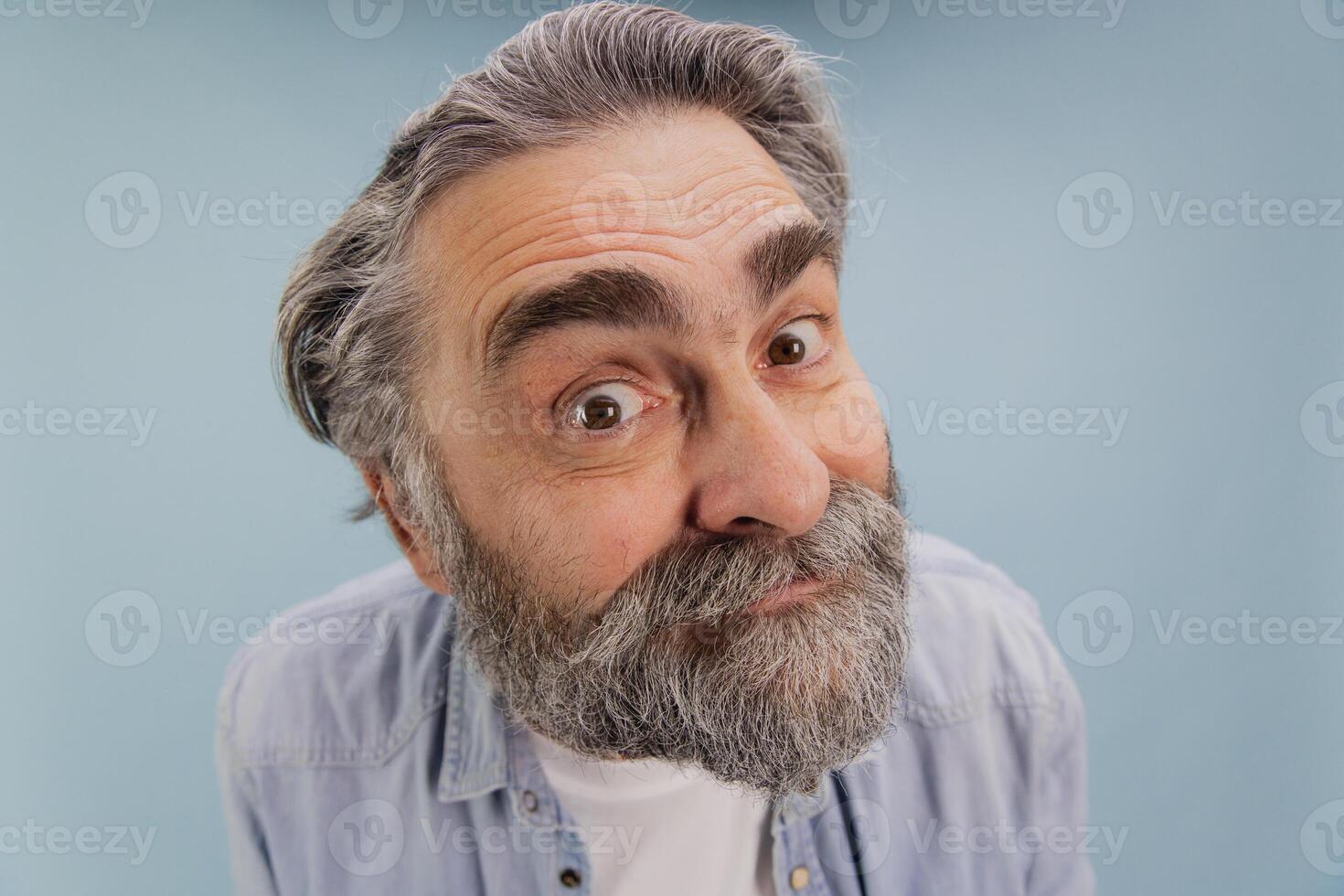 Curious senior man with grey beard and hair making a funny face on blue background photo