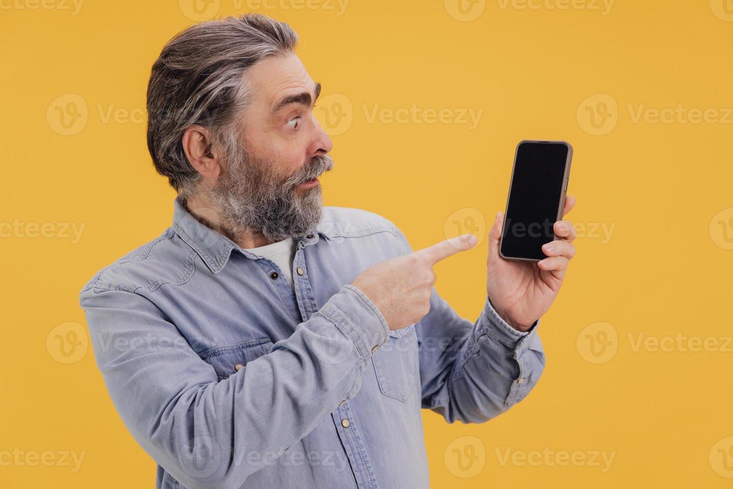 Surprised Senior Man Showing Smartphone with Blank Screen on Yellow Background photo