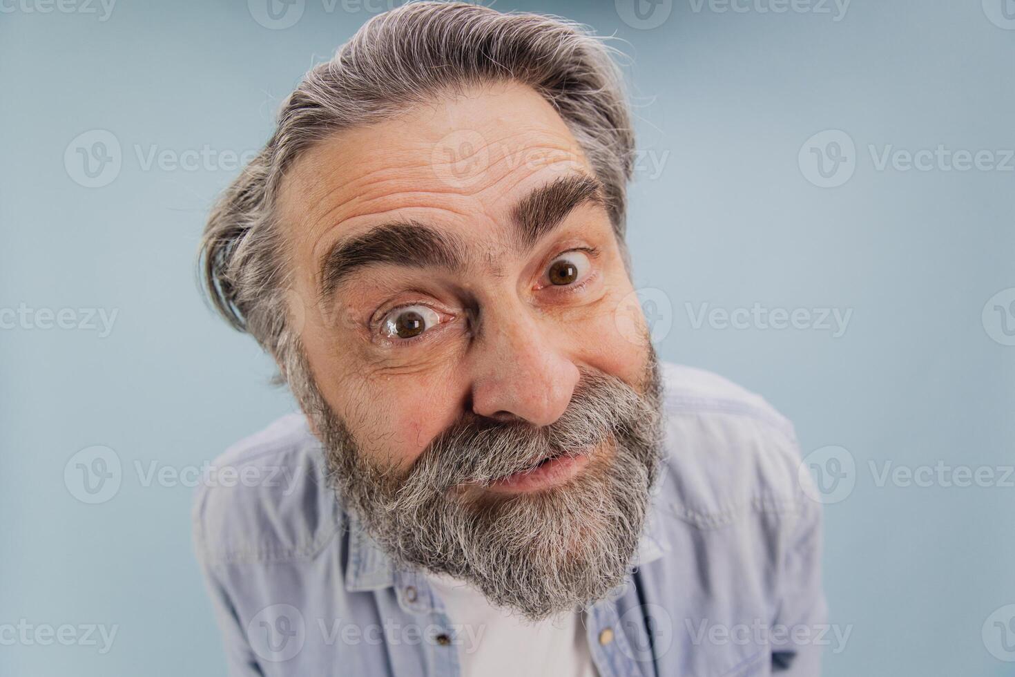 Curious senior man with grey hair and beard making funny face photo