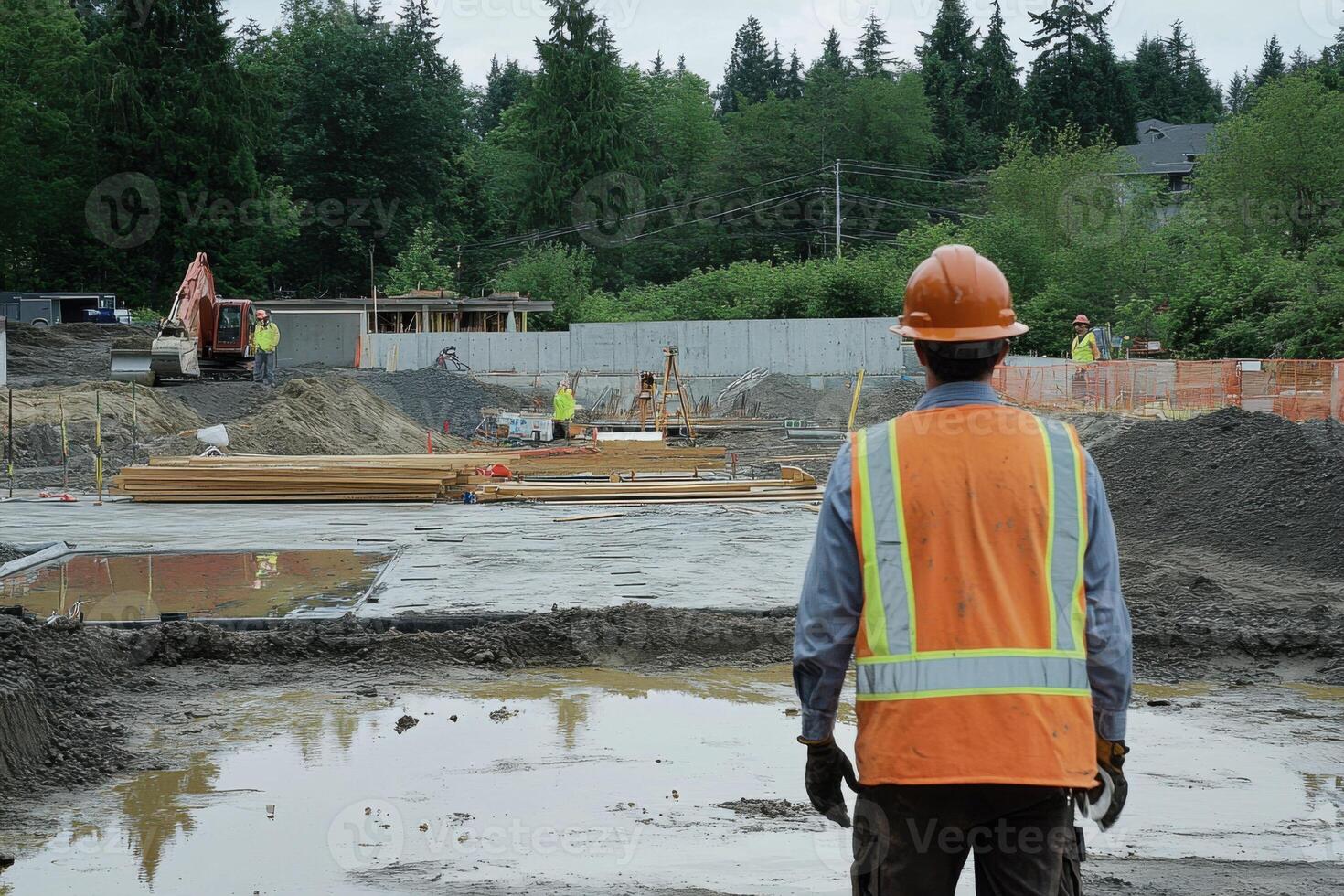 Construction worker oversees site in a residential area surrounded by trees and equipment on a cloudy day photo