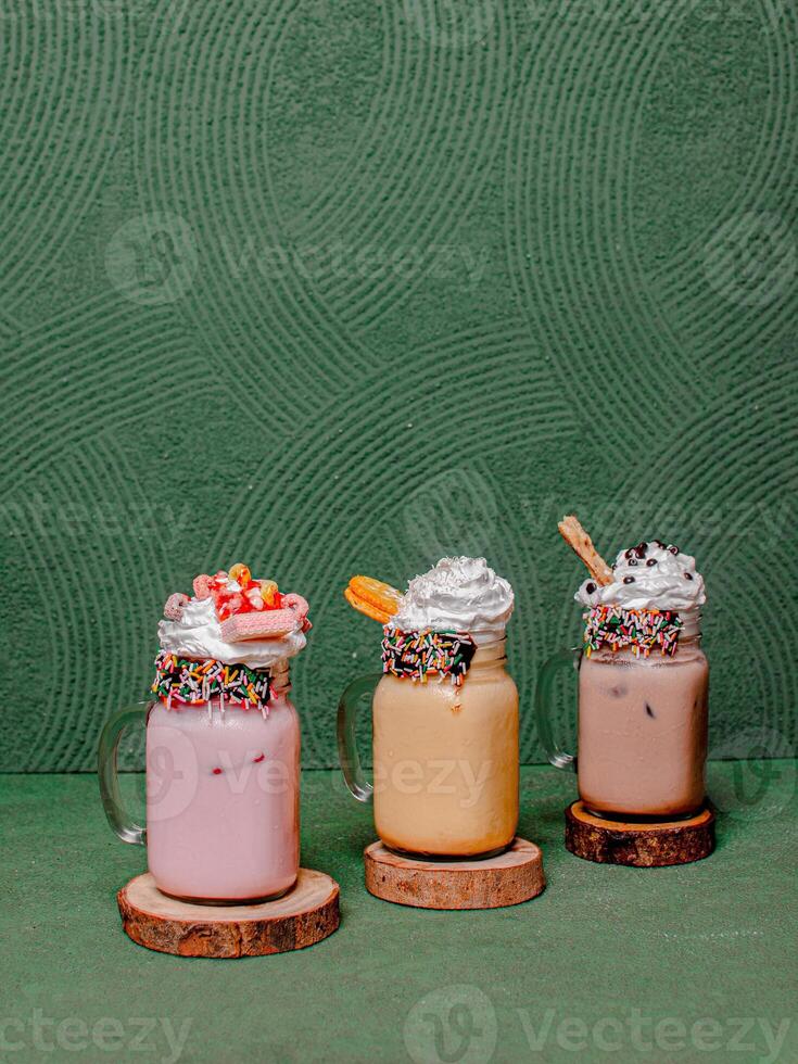 Delicious Strawberry, Mocha, And Chocolate Milkshakes With Whipped Cream And Toppings, Elegantly Served In A Glass On A Round Wooden Coaster. photo