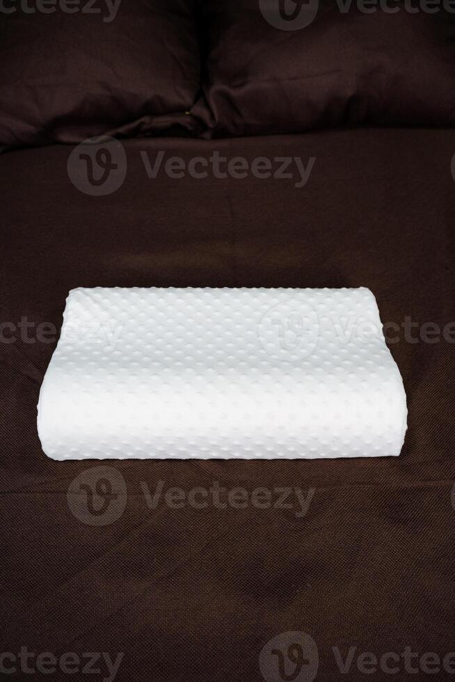 A white pillow on a bed with brown sheets photo