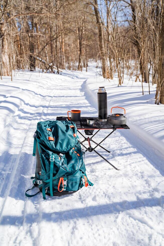 A backpack and a coffee pot sit on a snow covered path photo