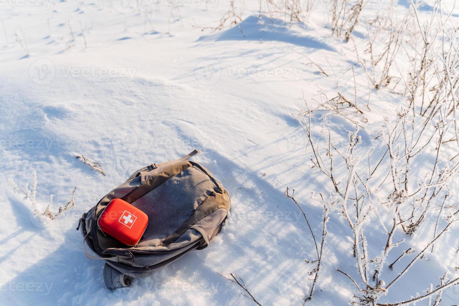 A backpack and red first aid kit on the ground in the snow photo