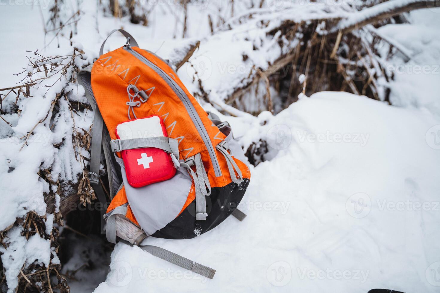 A backpack with an orange and red first aid kit on top of a snowy hill photo