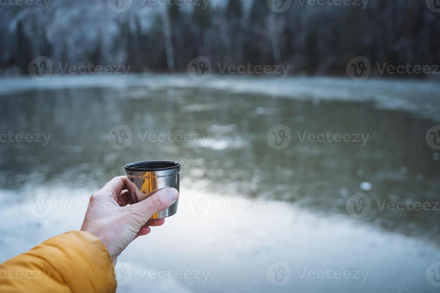 A person holding a cup of water in front of a lake photo