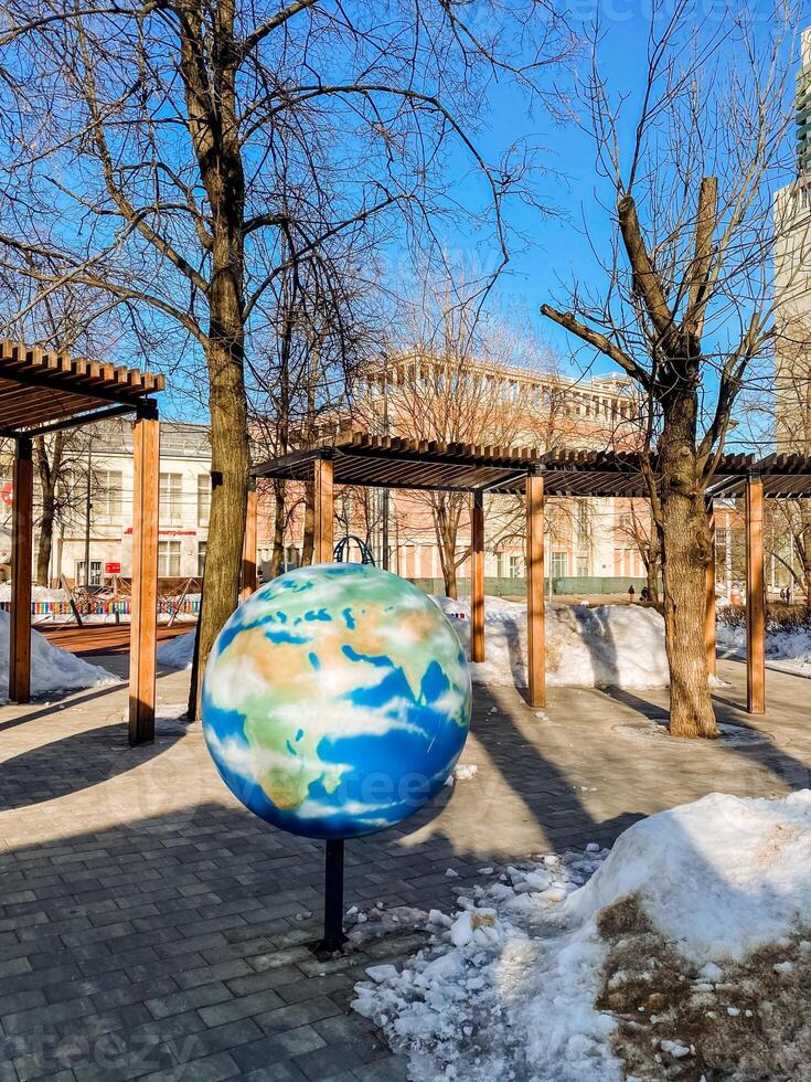 A globe sculpture in a park with trees and buildings photo