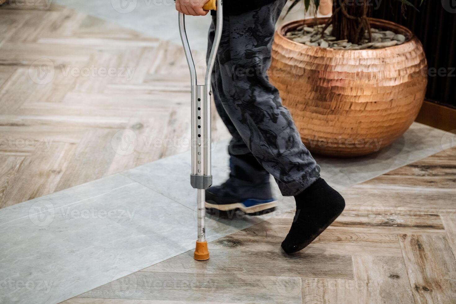 A person with crutches walking on a tile floor photo