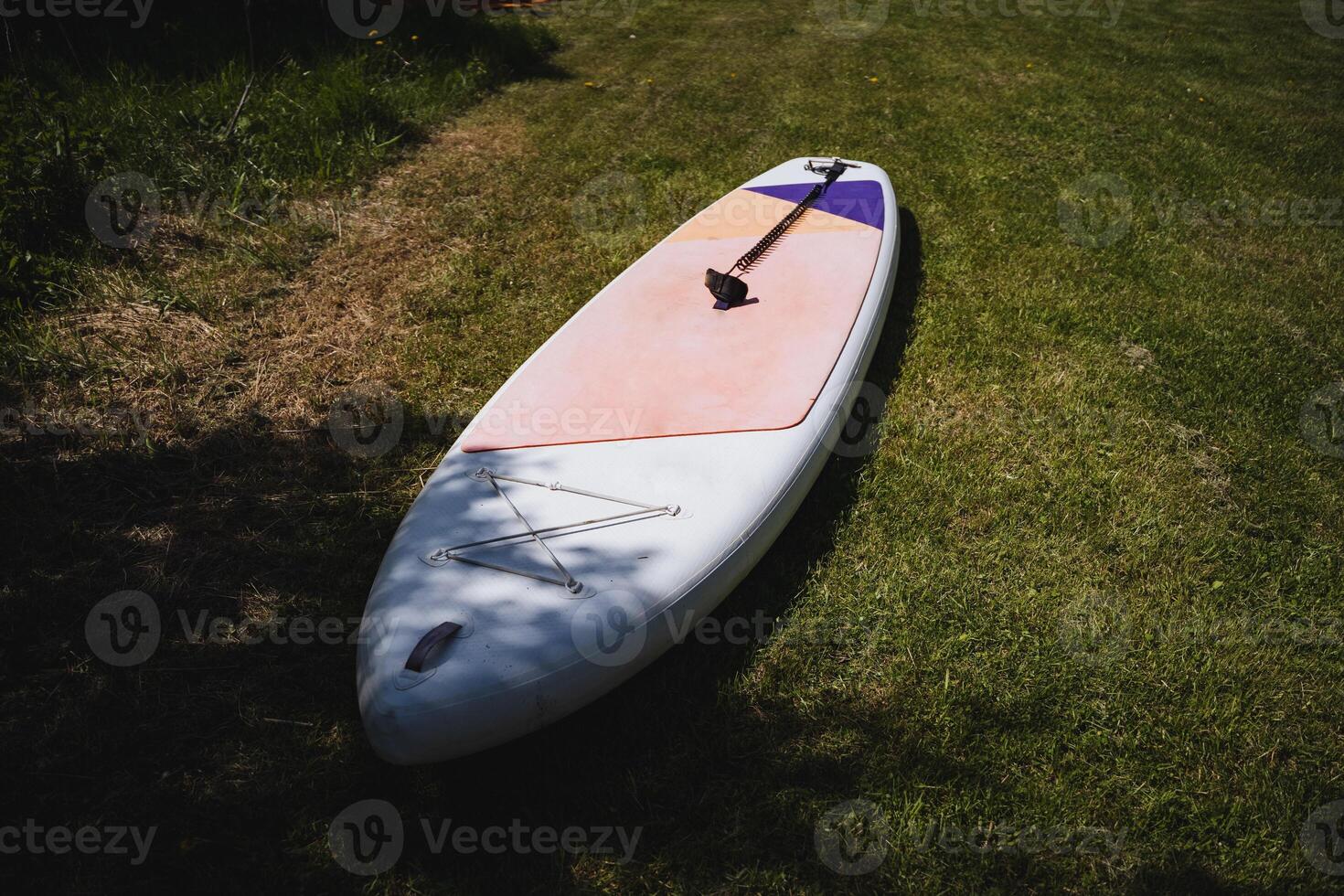 A white and purple surfboard laying on the grass photo