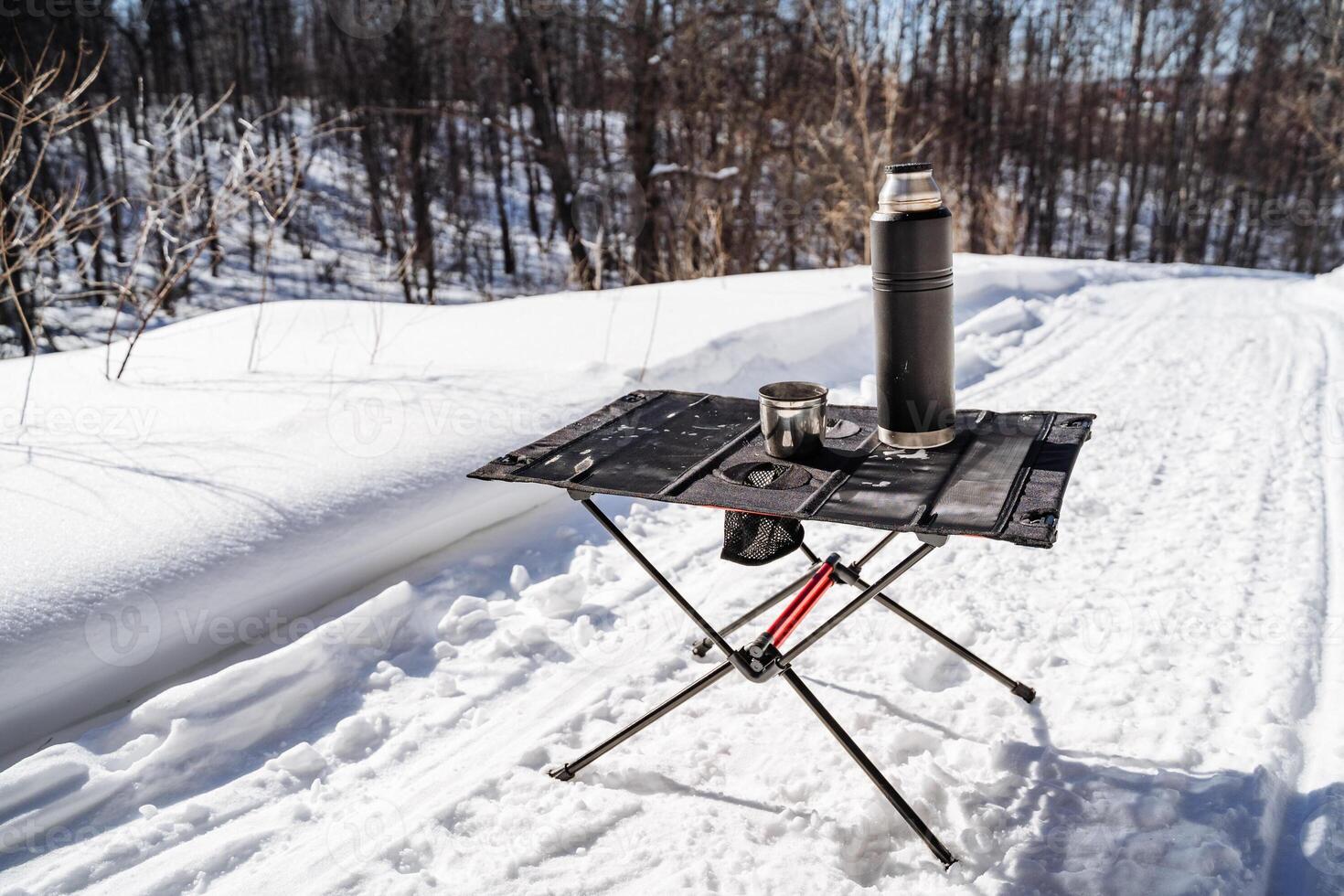 A camping table on a snowy road with a coffee pot and a cup photo