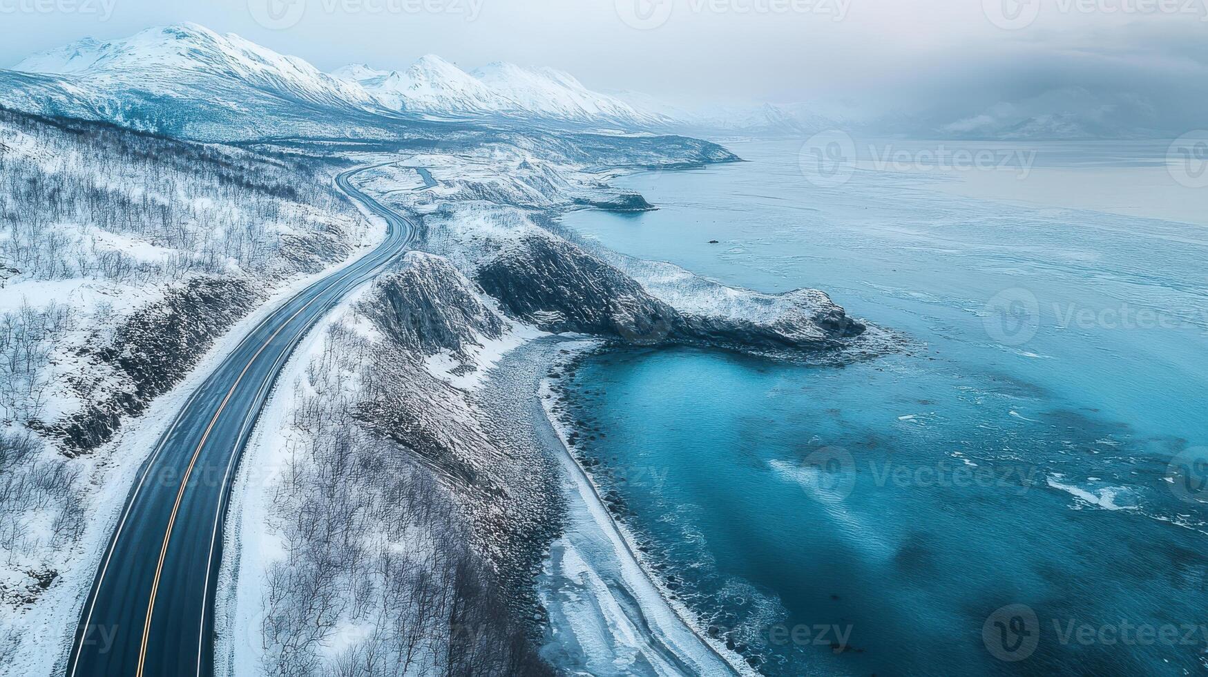 Winter road winding through majestic snow-covered mountains by icy ocean coastline photo