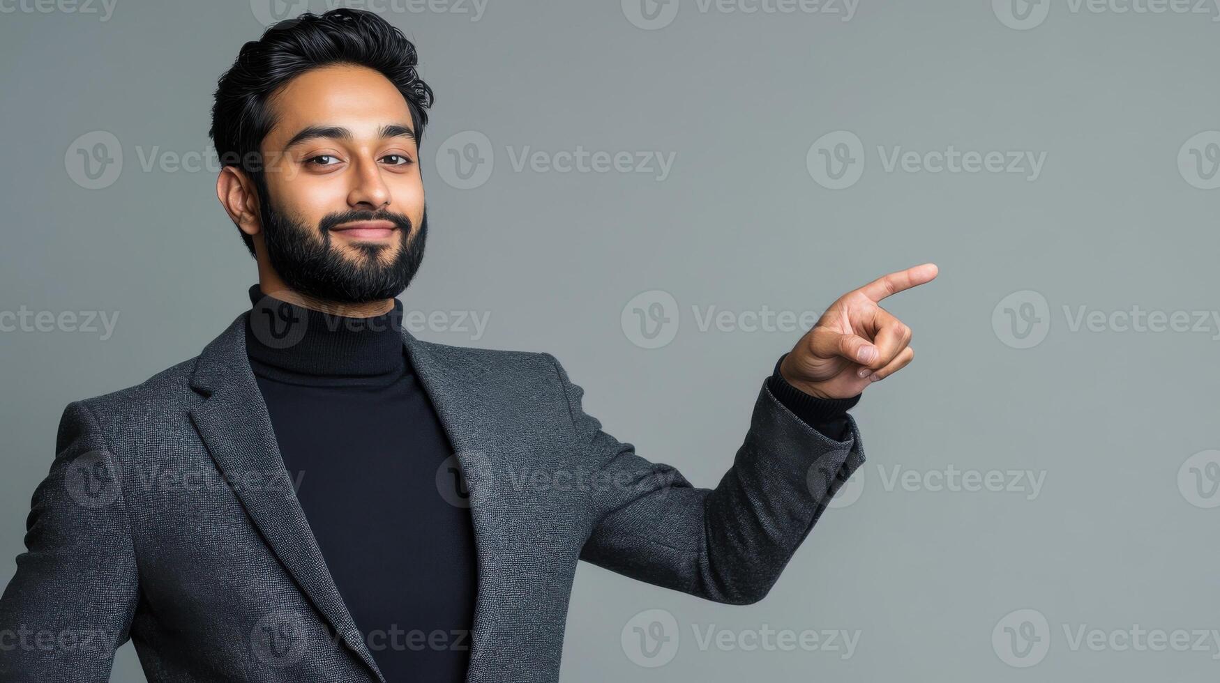 Confident young man in grey suit pointing at copy space on neutral background photo