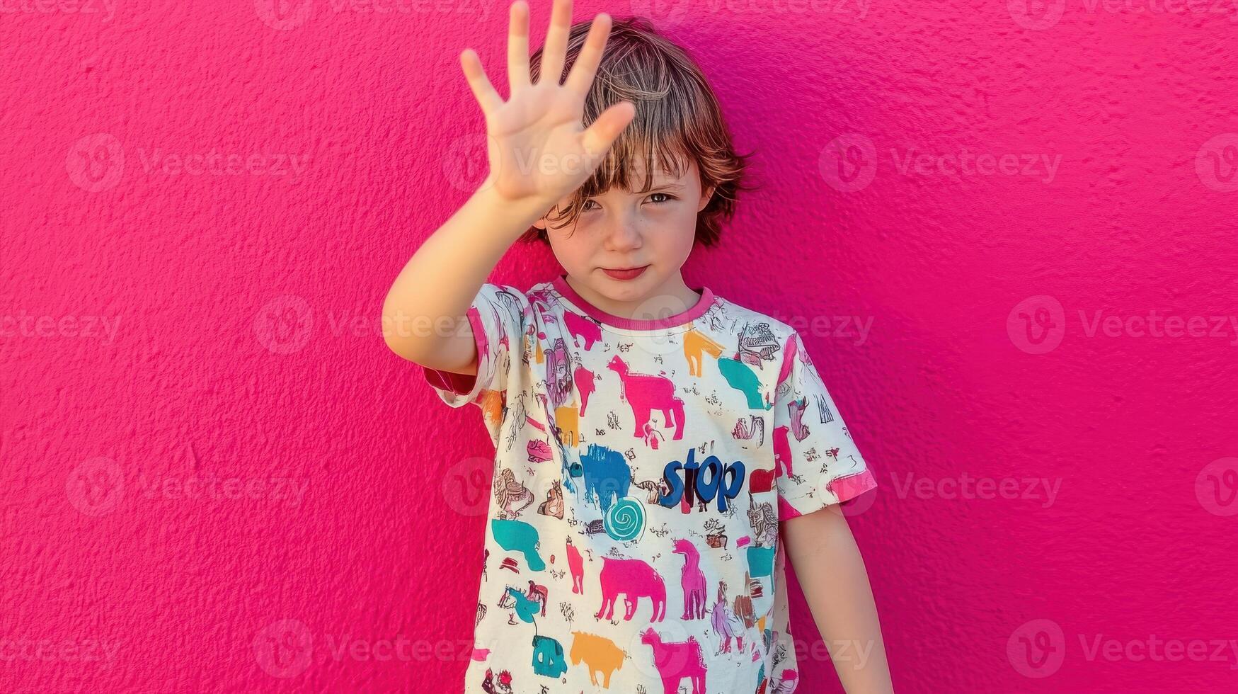 Young boy against vivid pink background raising hand for stop gesture photo
