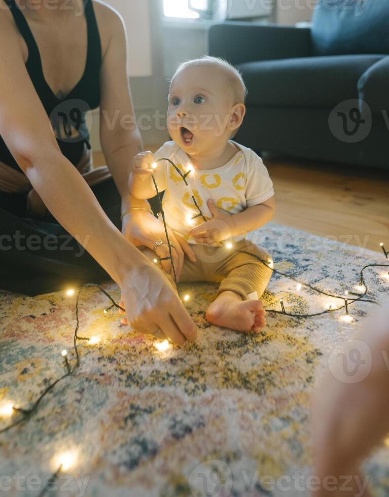 A Sweet Baby Joyfully Playing with Twinkling Christmas Lights in a Cozy Home Setting photo