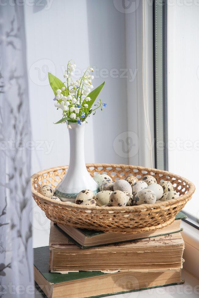 delicate small bouquet of lilies of the valley in a Chinese porcelain vase in the summer on a stack of old books on a windowsill, in a basket with quail eggs, Easter is coming soon, diet breakfast, photo