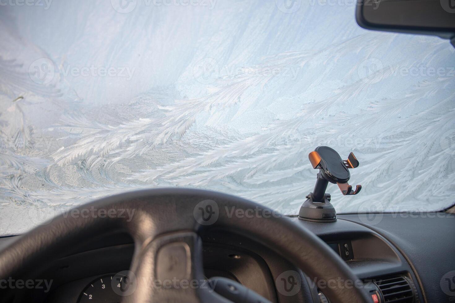 Frost patterns on car windshield at sub-zero temperatures, view from car interior on abstract winter pattern and dashboard, photo