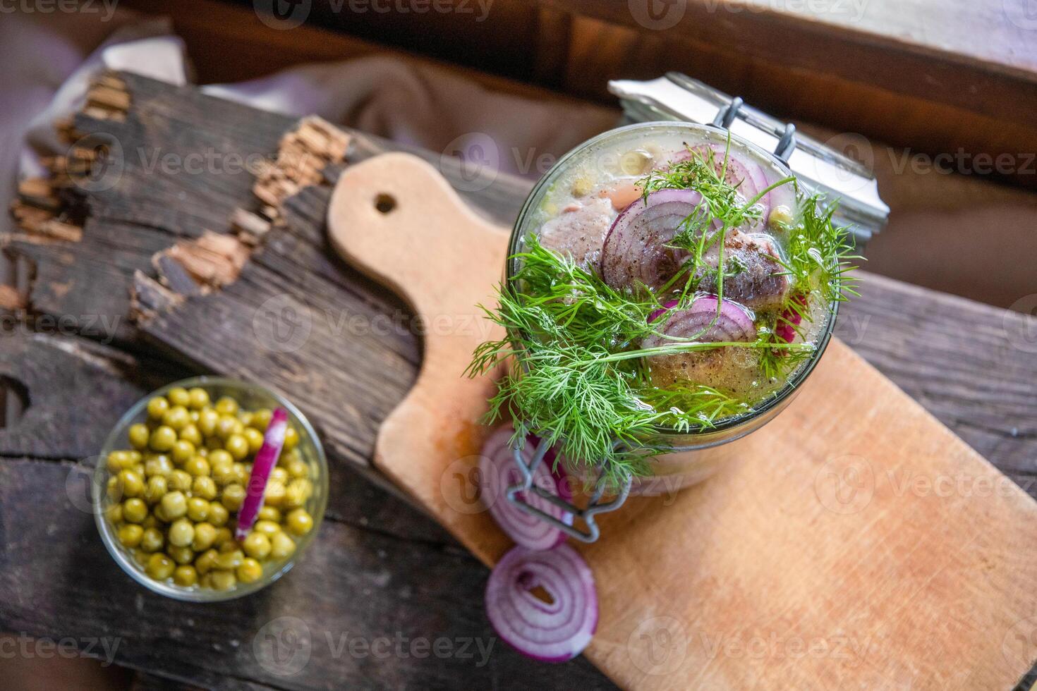 jar of marinated herring with onions in mustard sauce with dill and green peas on table, rural still life food photo, top view of composition on old wooden boards, photo