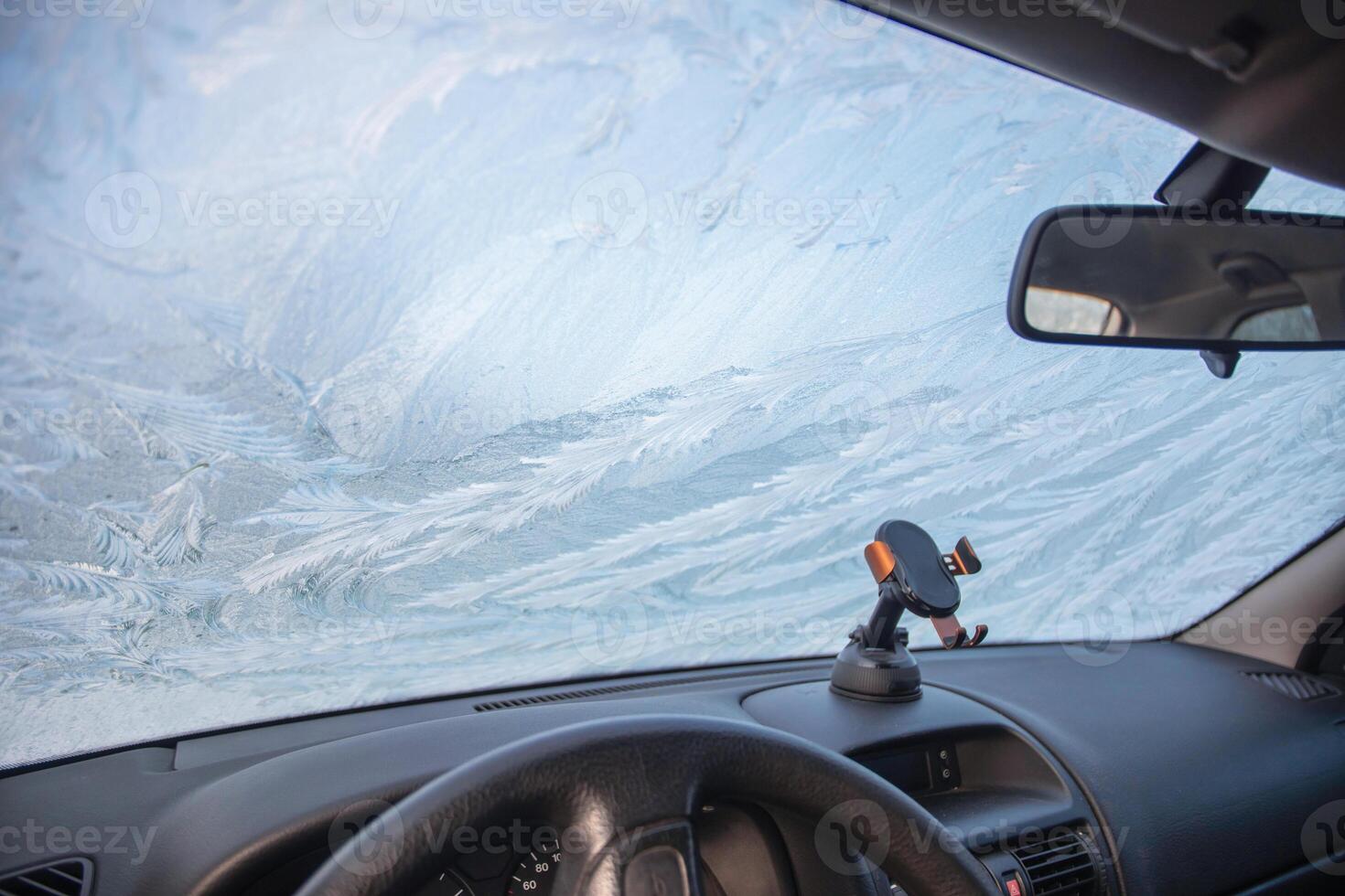Frost patterns on the windshield of a car at subzero temperatures, view from the car interior of an abstract winter pattern and the steering wheel of a car, photo