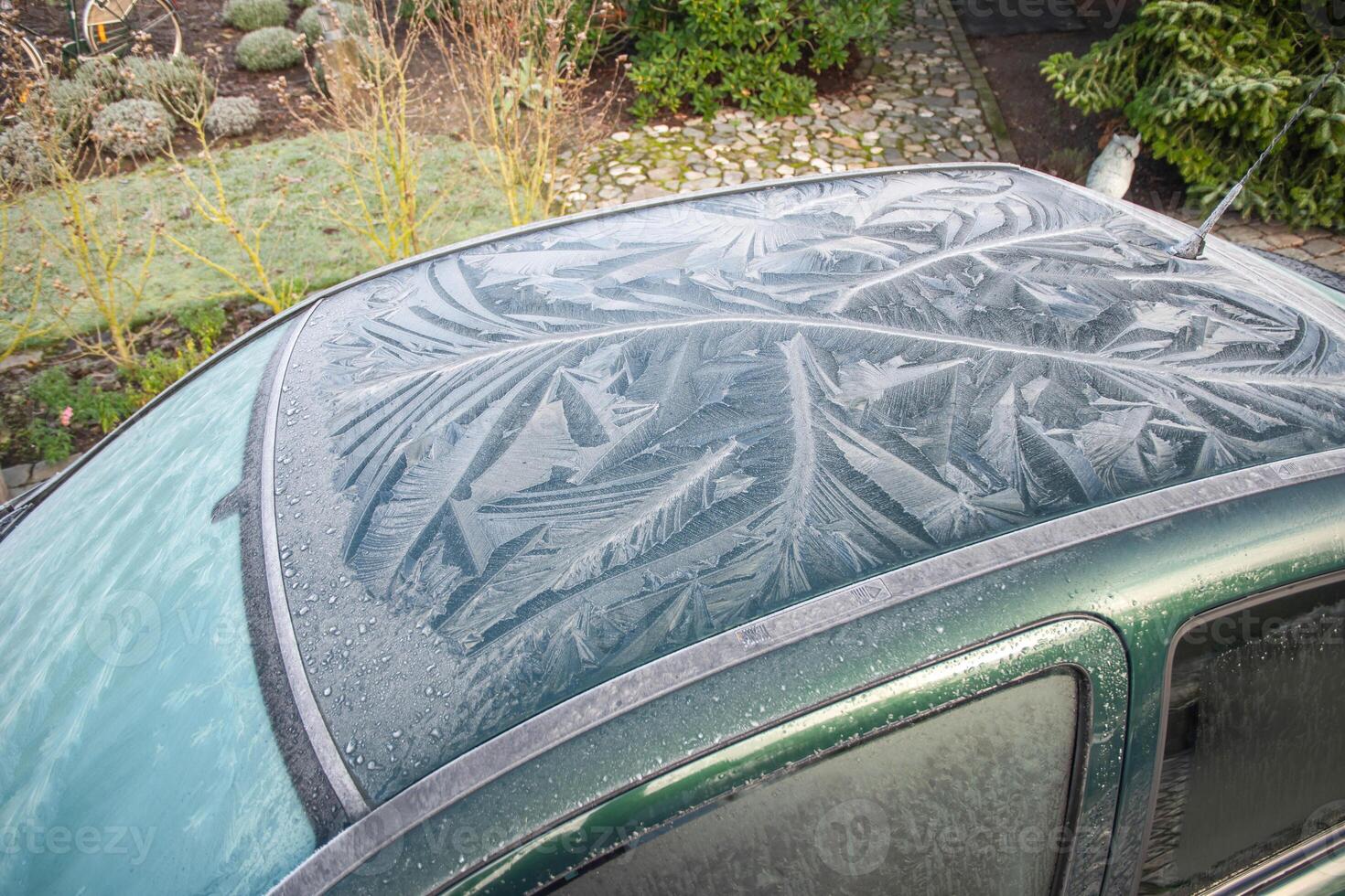 Nature drawings frost patterns on glass and roof of green car at air temperature below zero, abstract winter pattern, photo