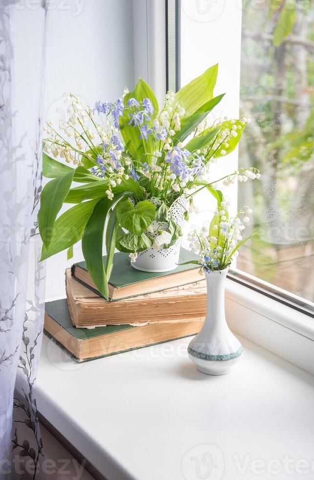 two bouquets of spring flowers on the windowsill, one of which stands on a stack of old books, lilies of the valley, creeping blue phlox,atmospheric scene, photo