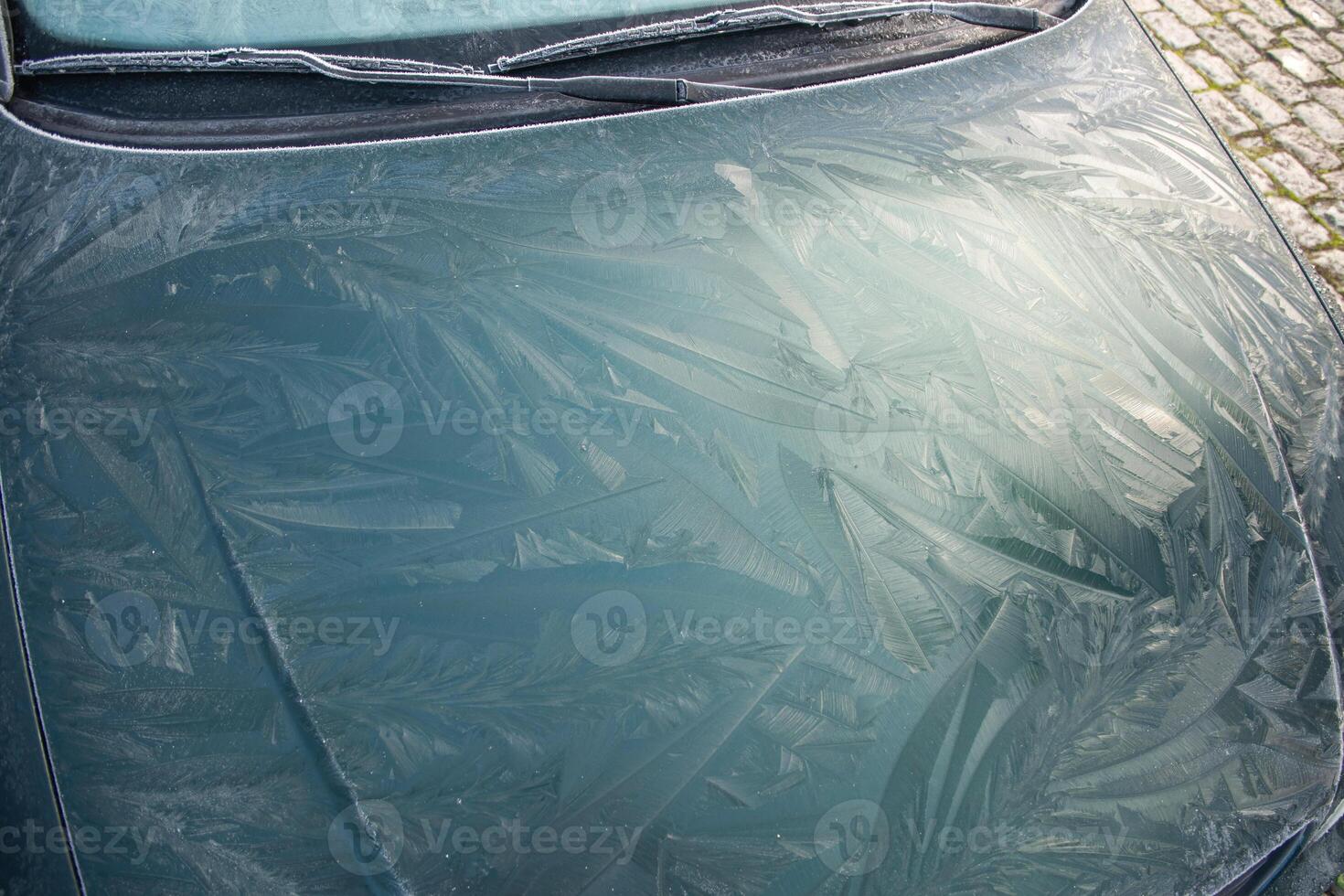 Drawings of nature frost patterns on the hood of a car at temperatures below zero, outside the car on an abstract winter pattern, photo
