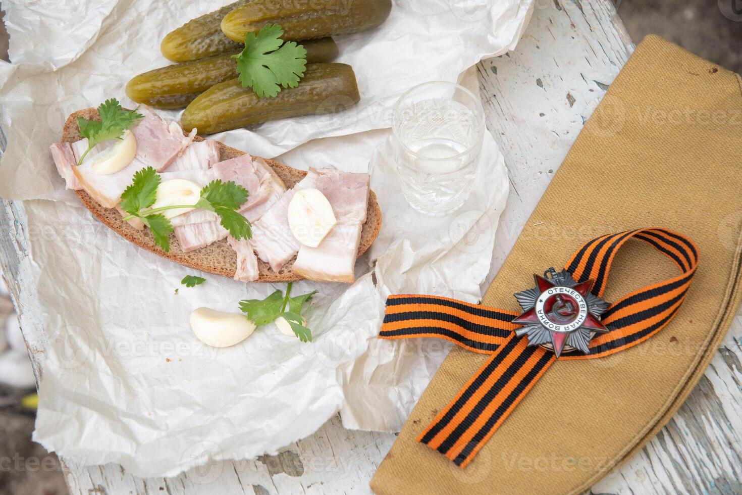 St. George's ribbon, Order of the Great Patriotic War, holiday May 9, Victory Day, still life on a shabby chair with glass of vodka and a snack of lard with garlic and pickled cucumber, photo
