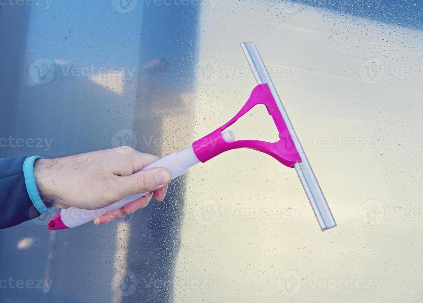 Male hand cleans glass window with Window Wiper Squeegee photo