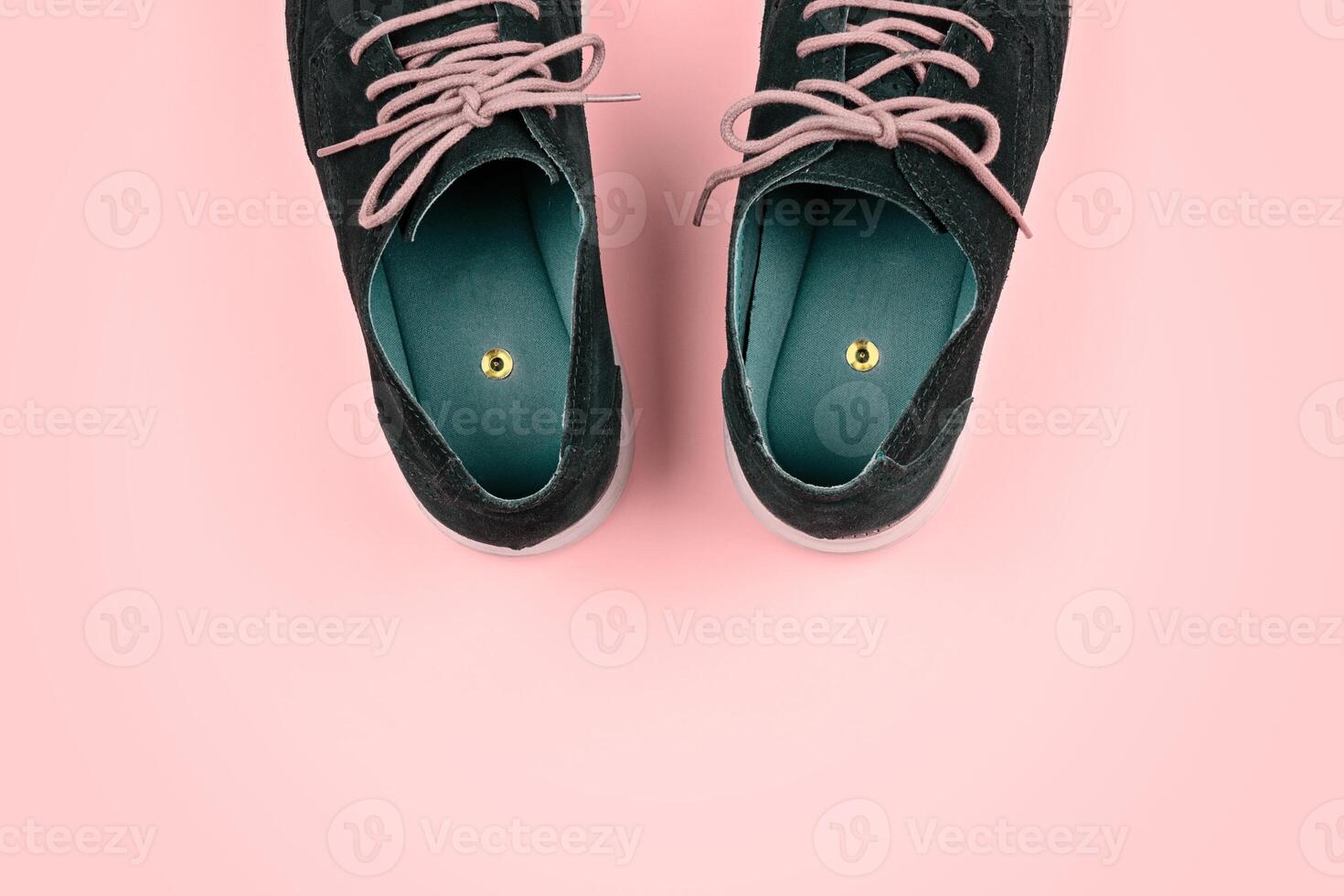 Pair of blue shoes with beige laces featuring push pin placed inside each shoe, against vibrant yellow background with copy space. Pranks and tricks concept photo
