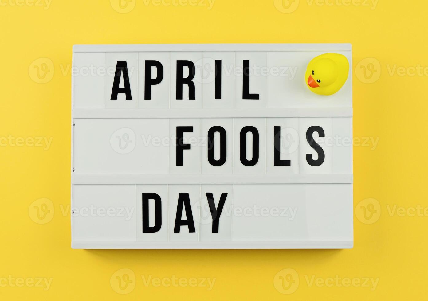 Lightbox Displaying April Fools Day With Green Leaves Against Bright Yellow Background, flat lay photo