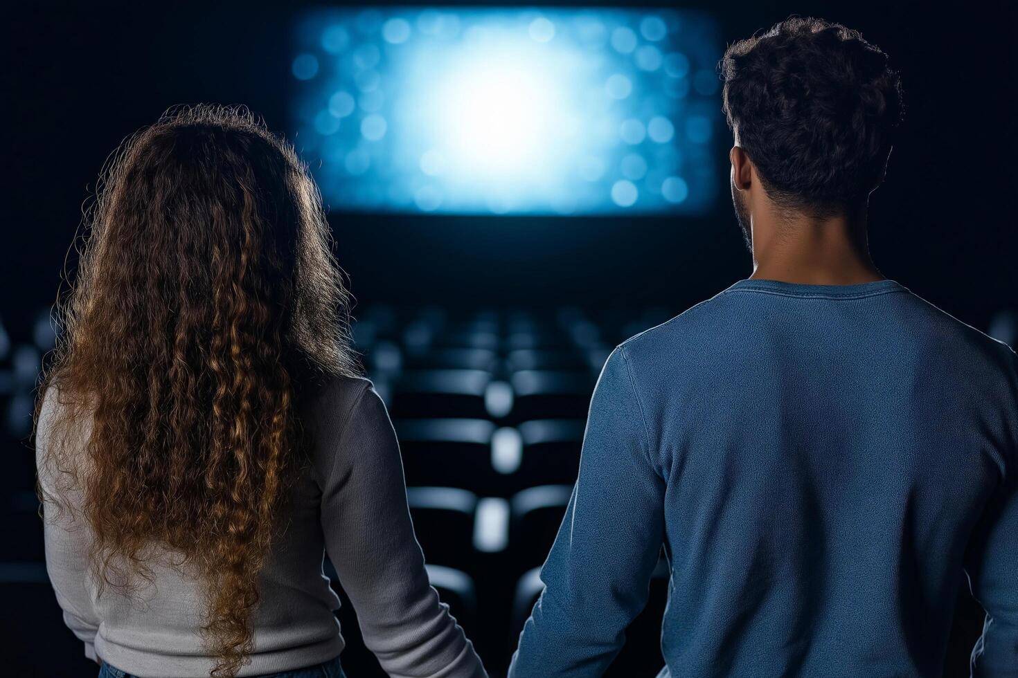 A romantic moment of a couple holding hands in a dimly lit movie theater, facing a glowing screen with a bokeh effect, creating a cozy and intimate atmosphere photo