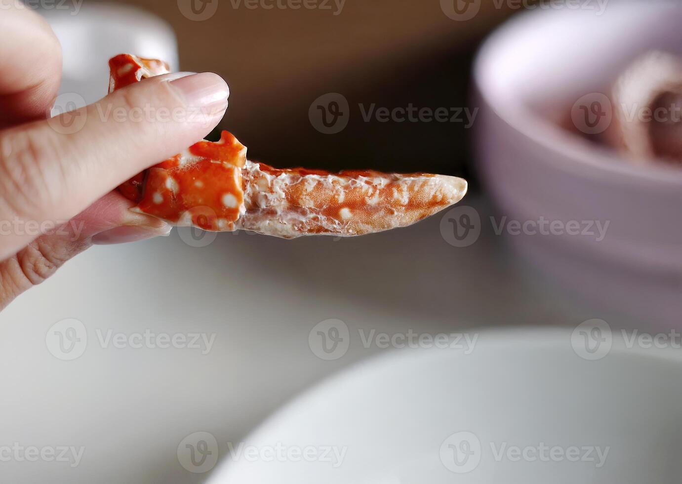 Female hand hold steamed peeled blue swimming crab leg, enjoying seafood meal with friends in local Thai restaurant, with blurred background photo