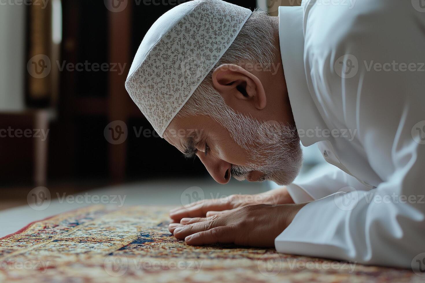 Elderly man in traditional attire praying on ornate carpet indoors photo