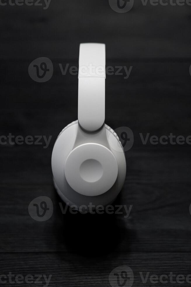 White over-ear headphones on a dark wooden surface, top view, minimalistic design, modern technology, isolated object, suitable for music and audio-related themes. photo