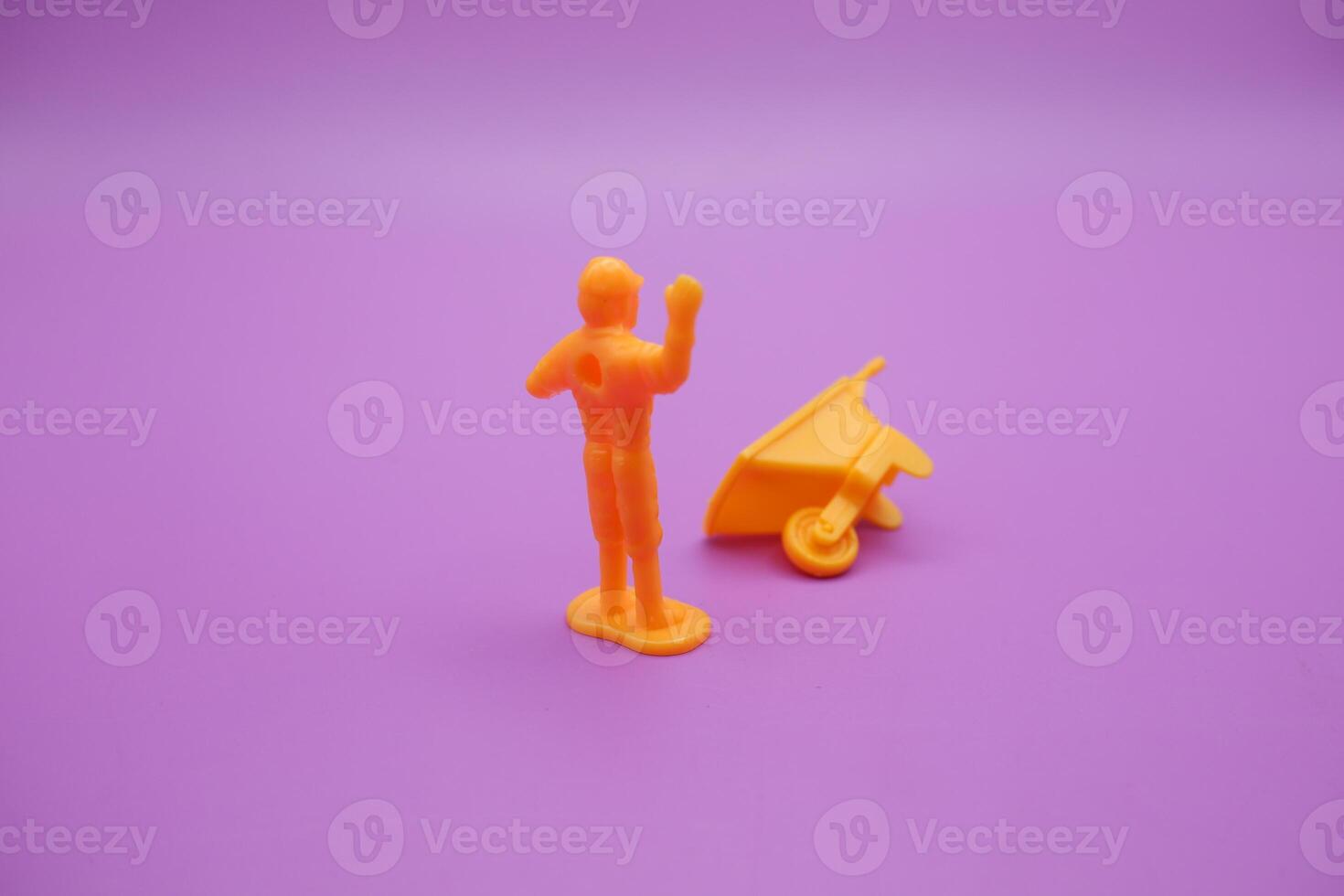 wheelbarrow toy and miniature worker isolated on purple background. yellow wheelbarrow and toy workers raising their hands. photo