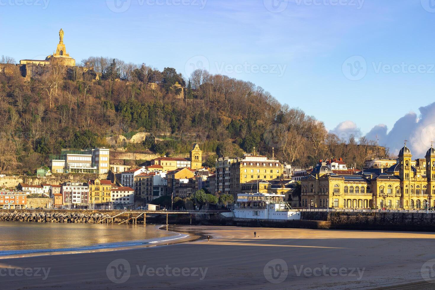 Sandy beach with waterfront buildings and hills in the background at sunset in San Sebastian, Spain. Coastal cityscape and natural landscape photo
