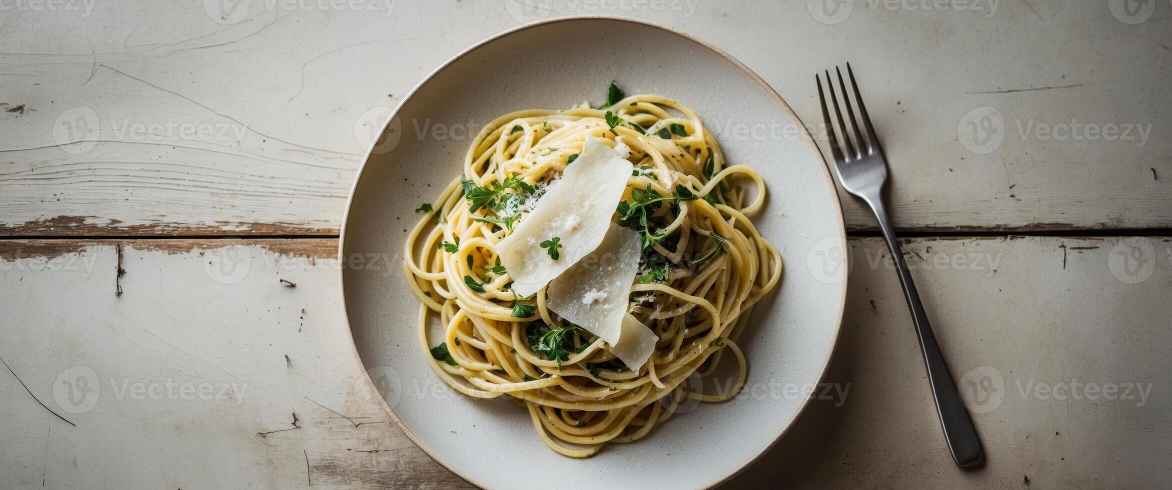 Freshly prepared spaghetti with herbs and cheese served on a white plate with fork on a rustic wooden table. photo
