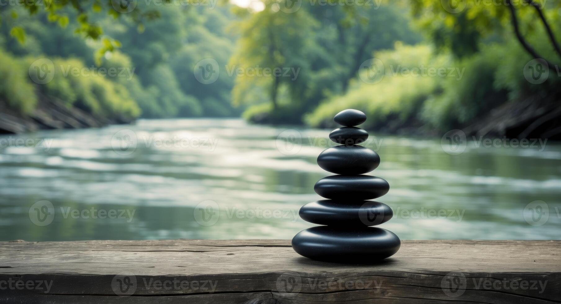 Stacked black stones on wooden surface by a tranquil river in a lush green landscape photo