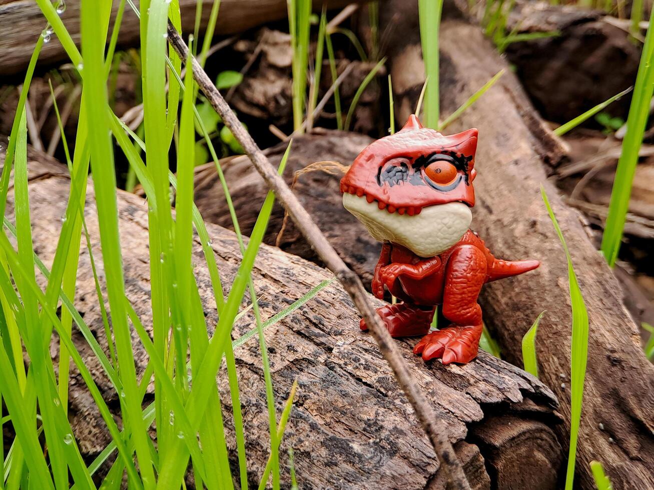 A toy dinosaur standing on a log in the grass photo