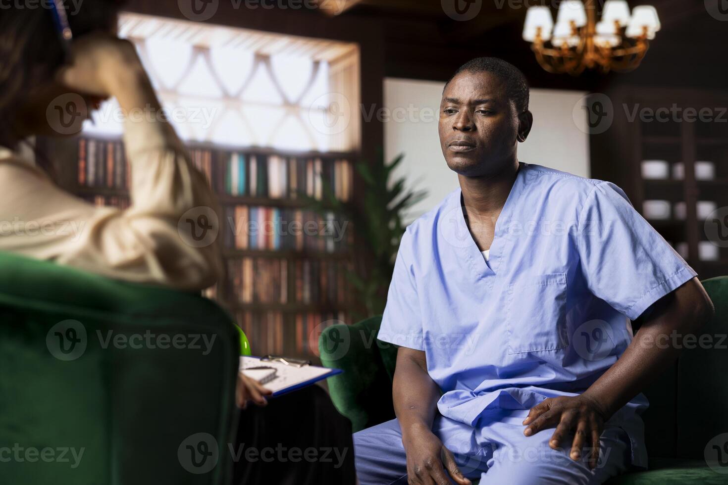 Nurse sits in serious counseling session coping with patients loss and mental health challenges. African american medical assistant working in a hospital with PTSD and trauma, powerless. photo