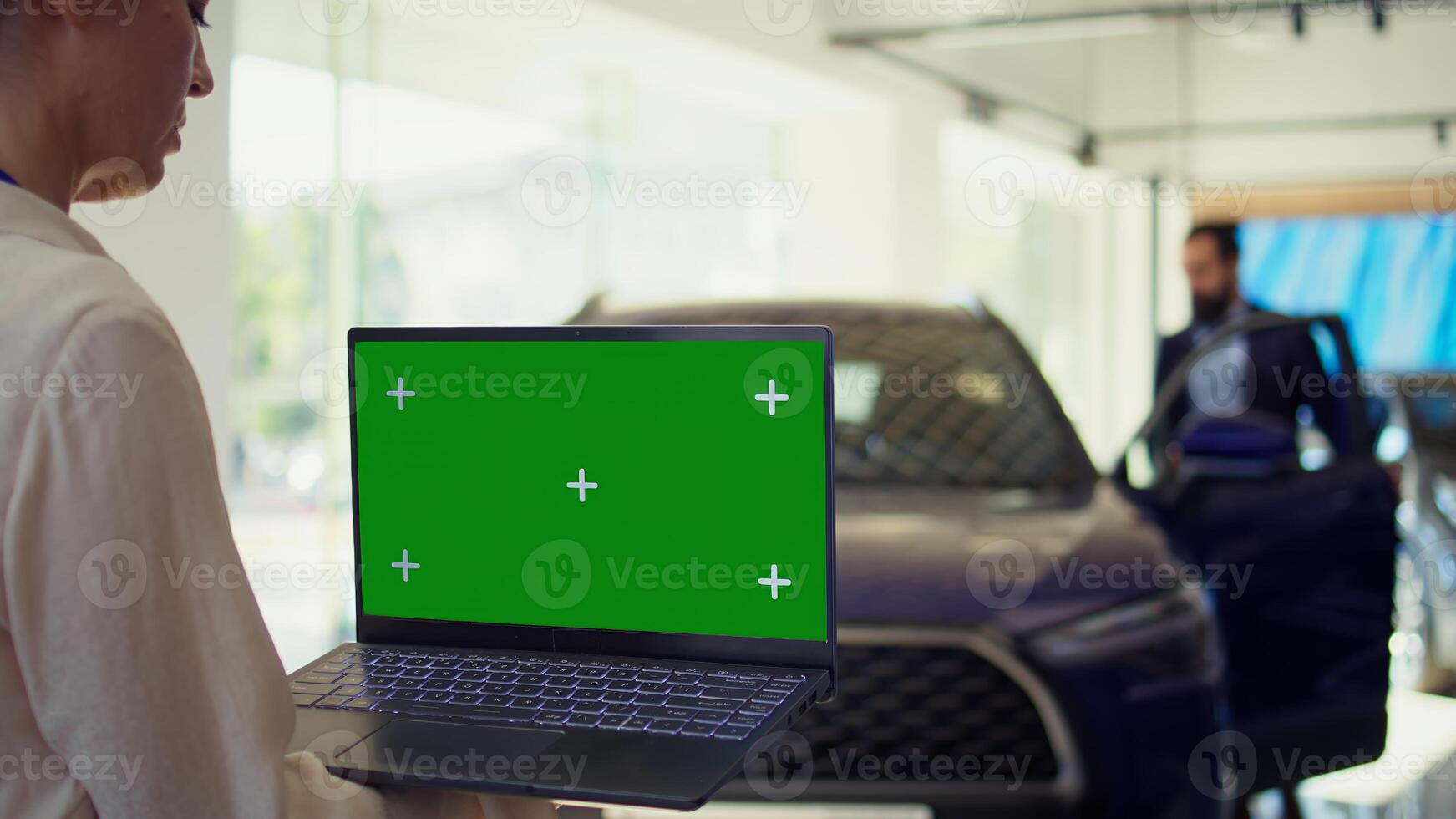 Customer in showroom looking for new vehicle to purchase or lease using green screen laptop. Woman evaluating automobiles in dealership before buying using chroma key notebook, camera B photo